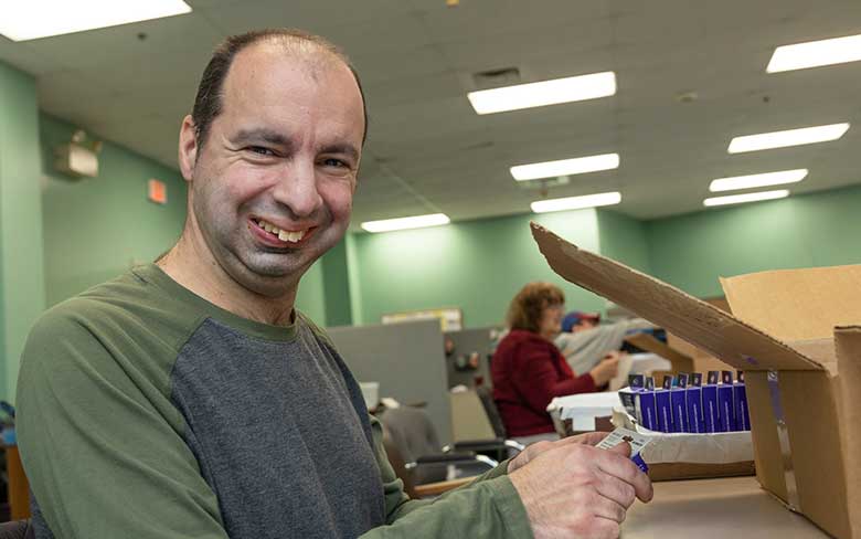 A man smiles at the camera while applying a sticker to a box as part of the Contract Packaging and Fulfillment services at Abilities