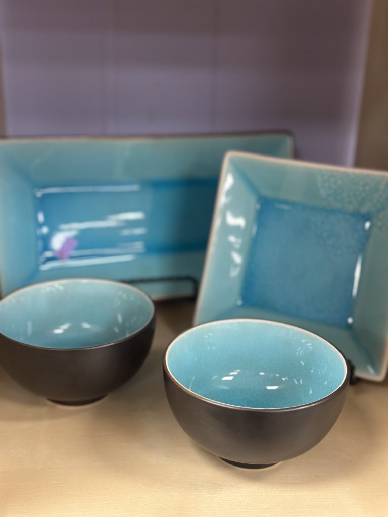 Set of turquoise ceramic dishware, including two round bowls and two square and rectangular plates, displayed on a light-colored surface.