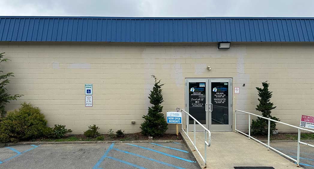Exterior entrance of the PossAbilities Thrift Phillipsburg location with accessible parking, a wheelchair-accessible ramp, and storefront doors displaying store information.